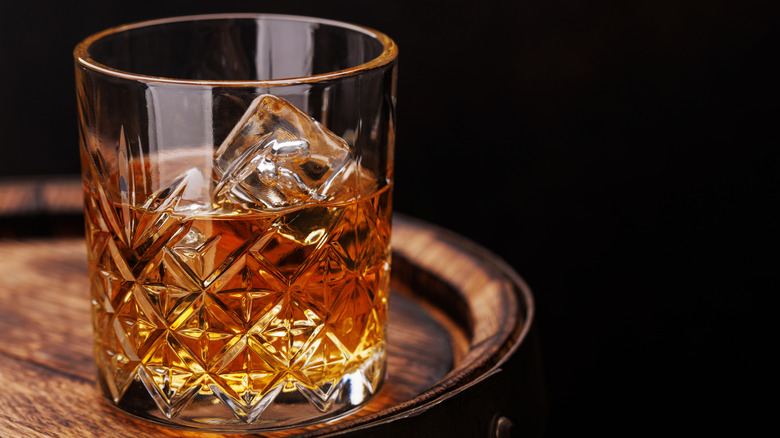 Whiskey glass with ice on a rustic barrel in front of black background