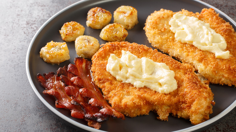 Breaded Chicken Maryland topped with a creamy white gravy served with bananas and bacon close-up in a plate on the table