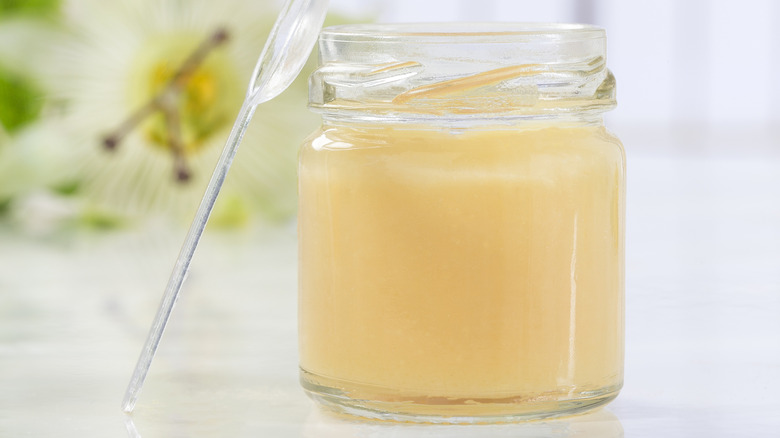 Light colored honey in glass jar in front of flowers