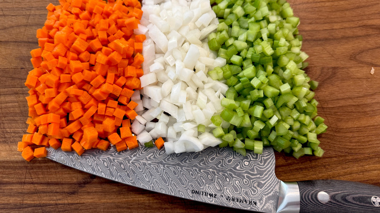 A kitchen knife and rows of diced carrot, onion, and celery for mirepoix