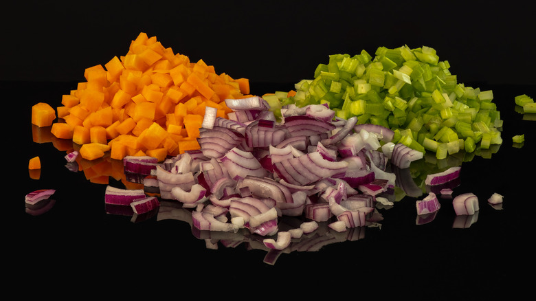 Three piles of dice carrots, onion and celery on a black background