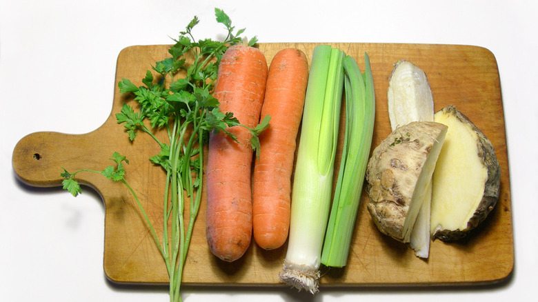 Carrots, leaks, celeriac, and fresh herbs on a wooden cutting board