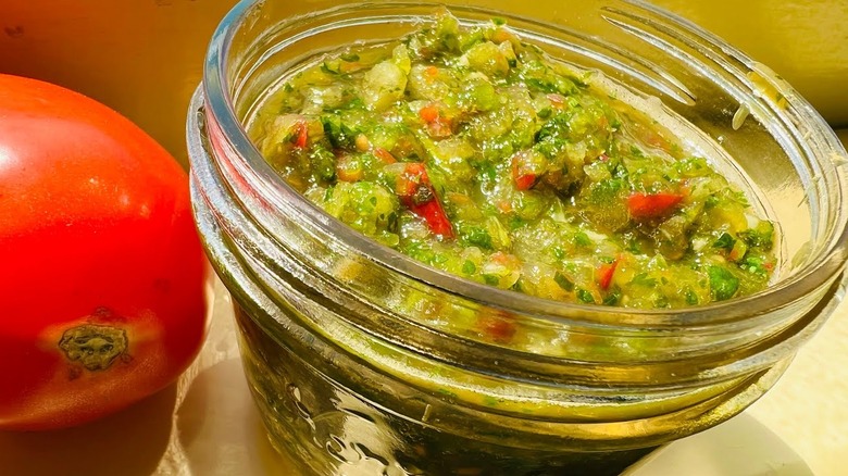 A jar of Rican recaito next to a whole tomato