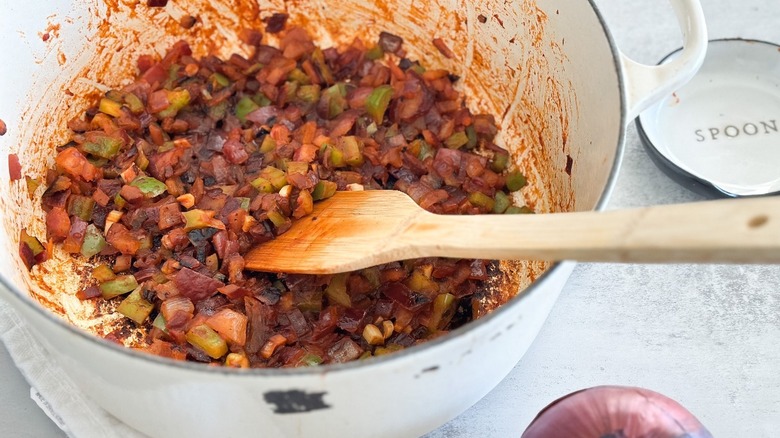 A wooden spoon in a large pot of Spanish sofrito