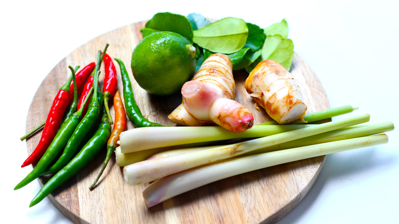 Chili peppers, kaffir lime and leaves, galangal, and lemongrass shoots on a wooden cutting board