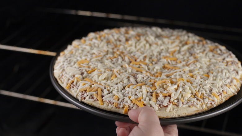 A hand placing a frozen cheese pizza into an oven
