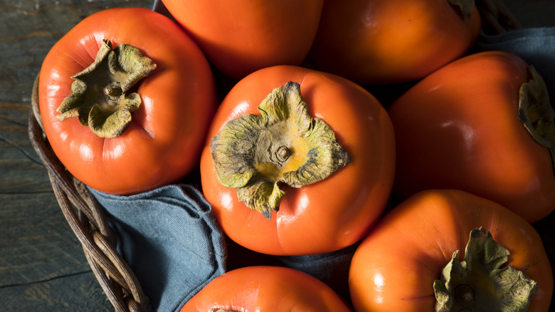 Fresh fuyu persimmons sit in a wooden basket.