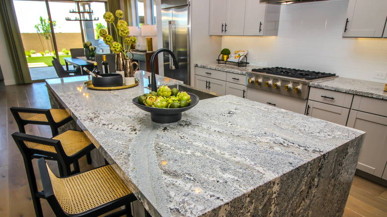A bright, open kitchen with gray marble countertops and a marble waterfall kitchen island