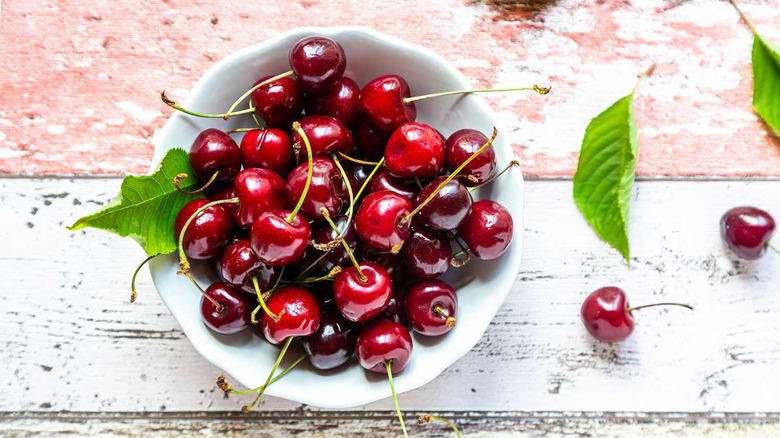 A white bowl of fresh red cherries on a table