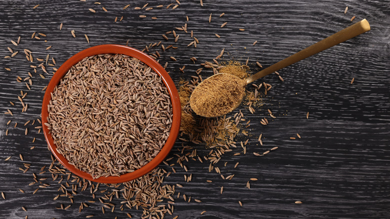 Topview of a bowl with whole cumin seeds and a spoon with ground cumin in it