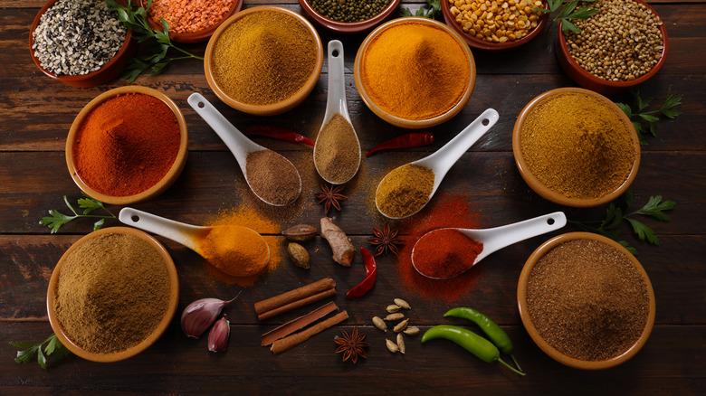 A selection of dried ingredients and spices in bowls and spoons on a wooden table