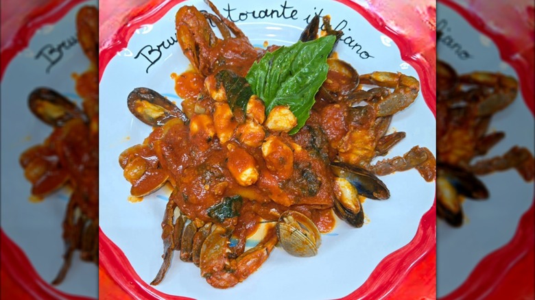 A crab and mussel dish in a red sauce on a red and white plate
