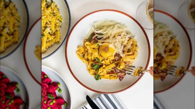A pasta dish with egg yolk on a bright table next to other colorful Italian dishes