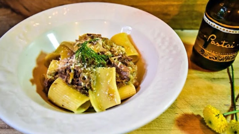 Paccheri alla genovese in a white dish next to a Pastai-branded bottle