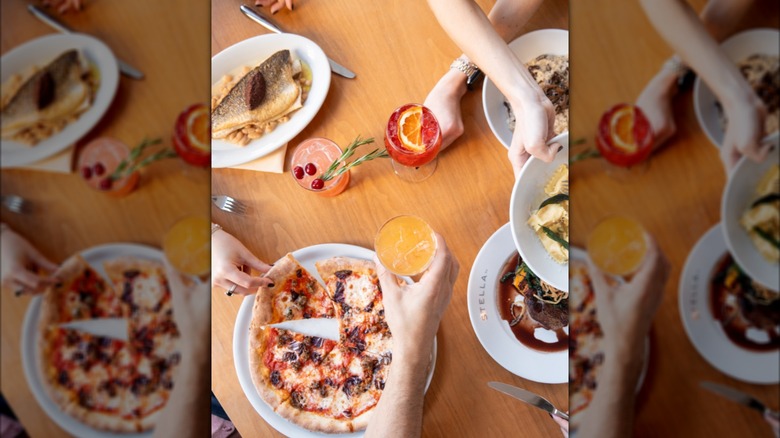 Top view of friends sharing Italian dishes and colorful coktails on a light wood table