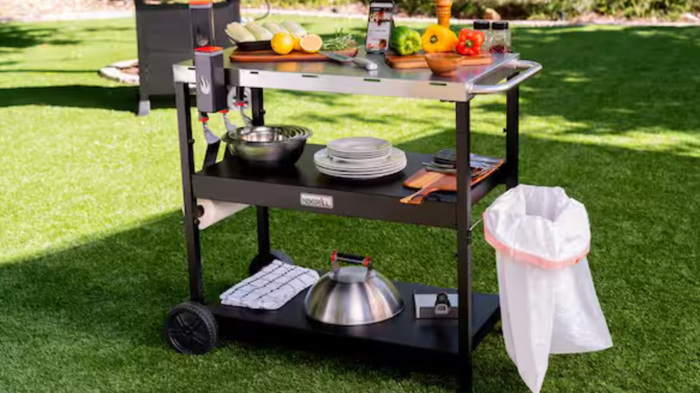 Nexgrill Stainless Steel and Black Grill Cart loaded with plates and food in a backyard