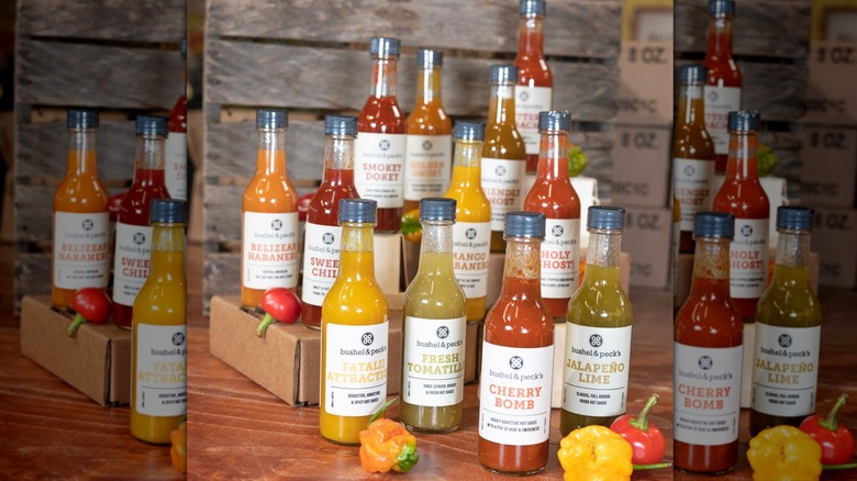12 bottles of Bushel & Peck's hot sauce arranged with a gift box and small hot peppers