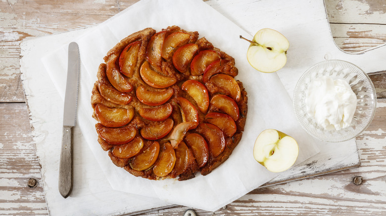 Tarte Tatin on table next to apples, cream, and knife