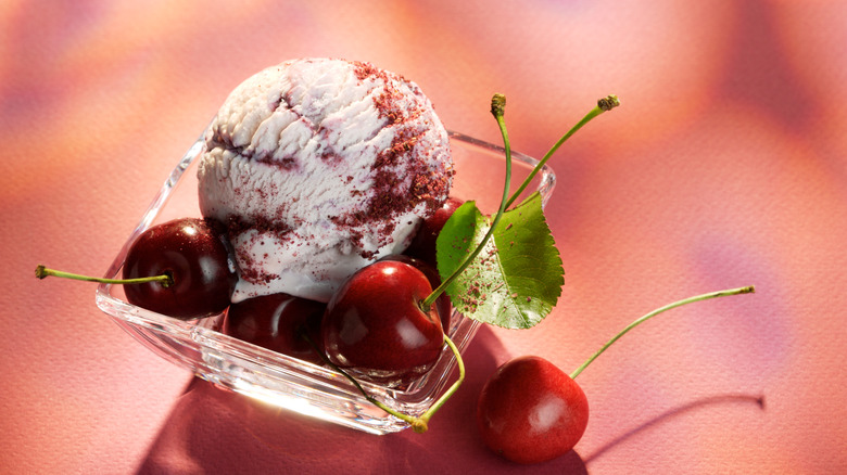 One scoop of cherry ice cream in a glass bowl with cherry garnishes
