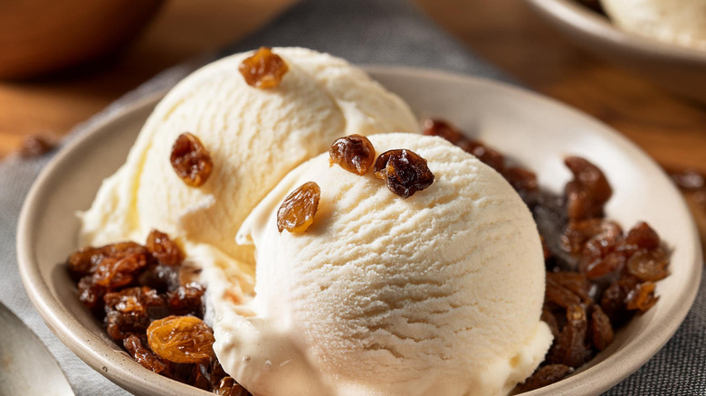 Two scoops of rum raisin ice cream in a bowl topped with raisins