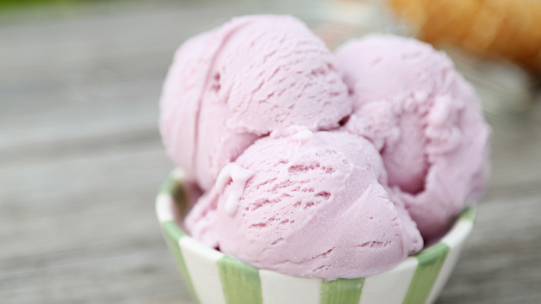 Three scoops of strawberry ice cream in a green and white striped bowl