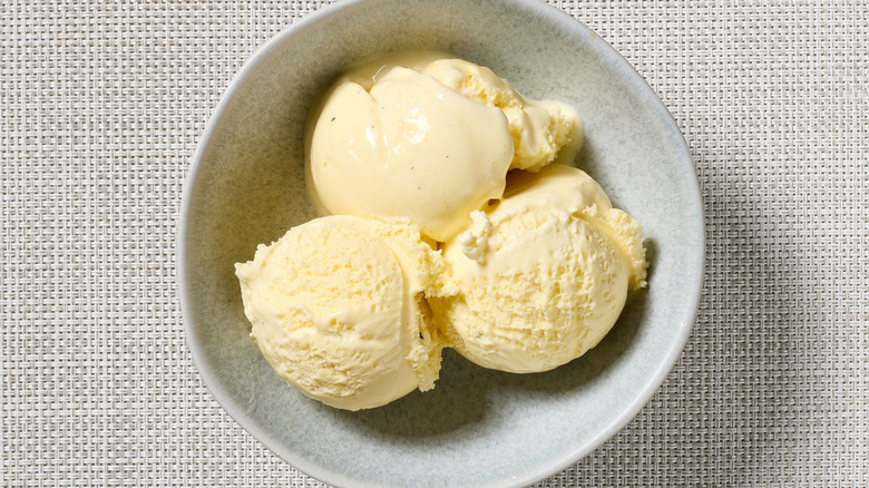 Three scoops of vanilla ice cream in a bowl on a white woven table mat