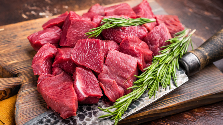 Raw venison chunks on a cutting board with knife and rosemary