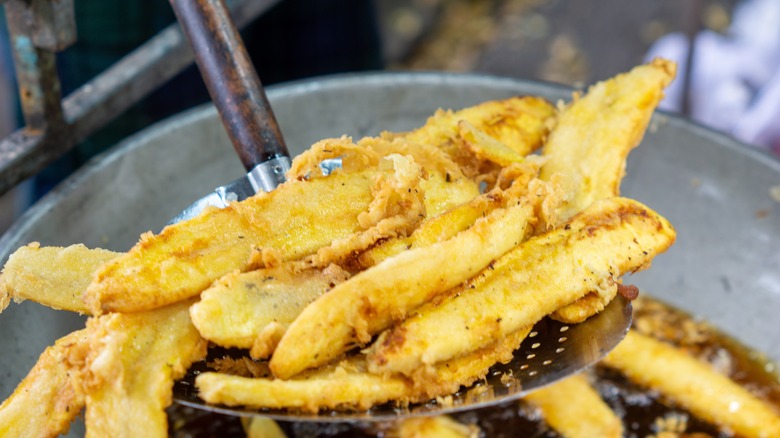 Spooning Pisang Goreng deep-fried bananas out of hot oil
