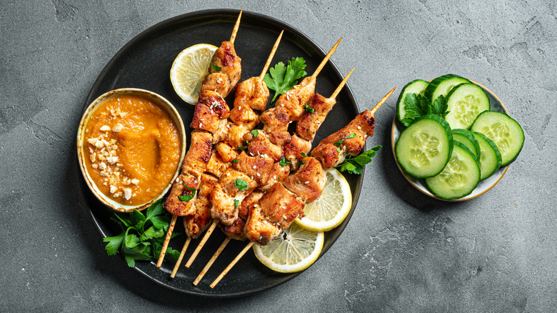 Plate of satay chicken skewers with lemon and cucumber slices