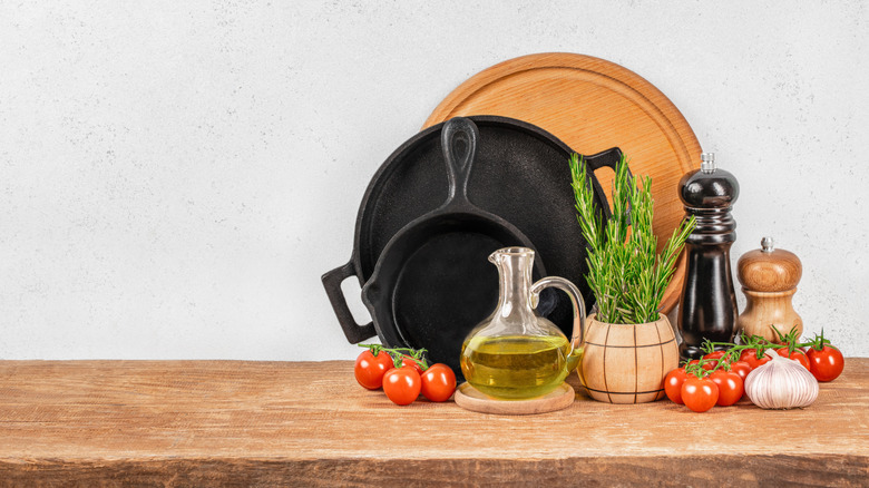 Rustic kitchen scene with cast iron pans, fresh herbs, vegetables and pepper mills against a light backdrop