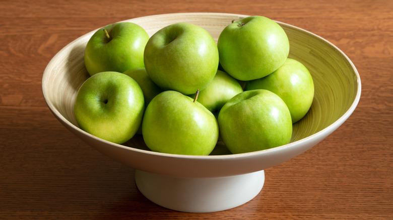 Granny smith apples in a white bowl on a wooden table