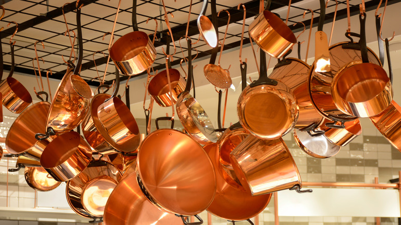 An assortment of copper pots and pans hanging from a ceiling rack