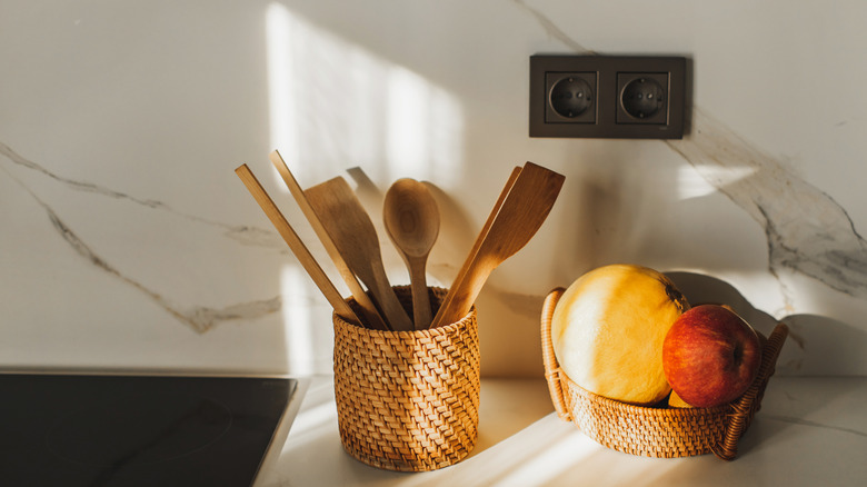Wooden spoons and fruits stored in rattan baskets against a white countertop