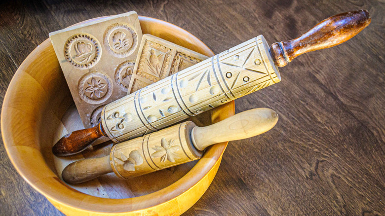 A wooden bowl holding a set of carved vintage rolling pins