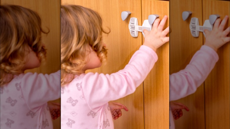 Toddler trying to open a child lock on a brown cupboard door