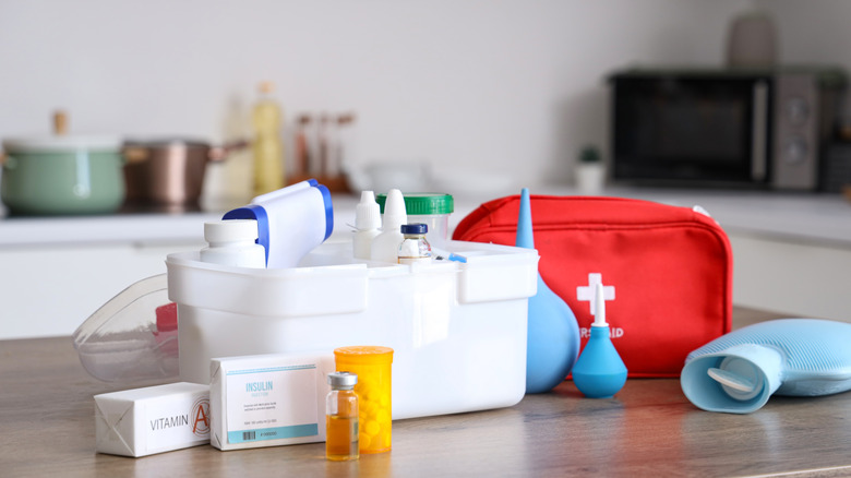 The contents of a First AId Kit on a kitchen counter includes medication, and a hot water bottle