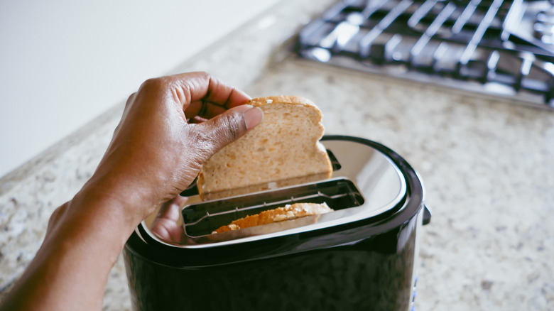 Close up of a person putting a slice of brown bread into a toaster