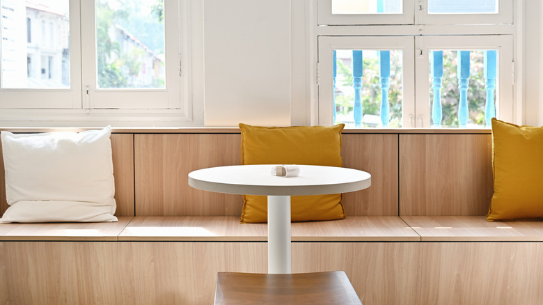 Wooden banquette seating with white and yellow cushions behind a white table