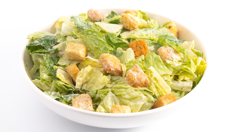 A Caesar salad with croutons in a white bowl
