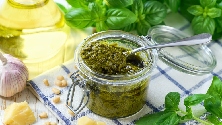 A glass jar of pesto next to garlic and basil