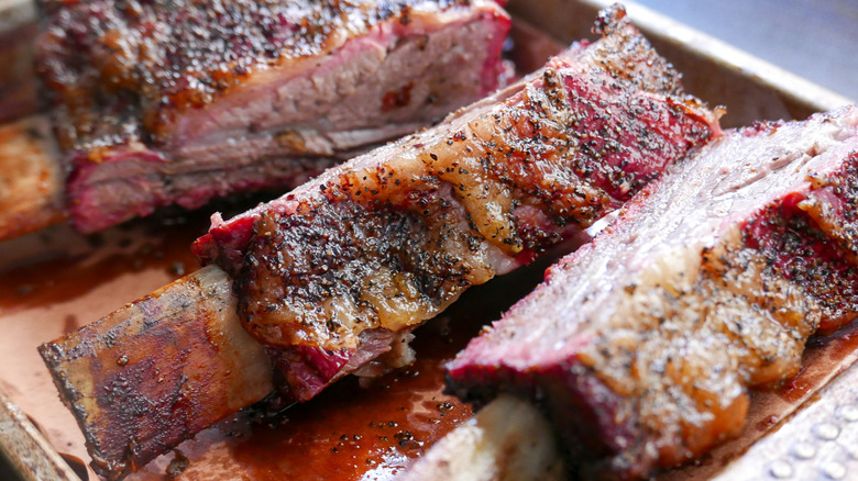a close-up of cooked beef ribs with cracked black pepper on top in a pan