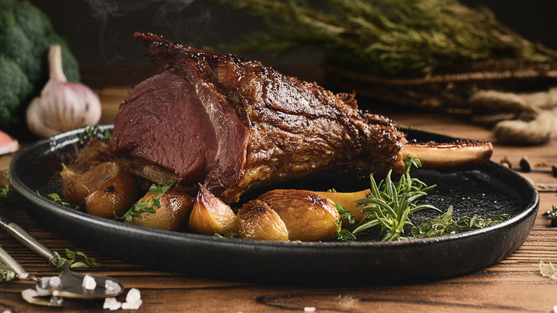 a roasted leg of lamb with potatoes and herbs on a platter