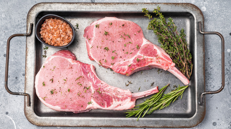 raw pork chops on a metal platter with herbs and rock salt