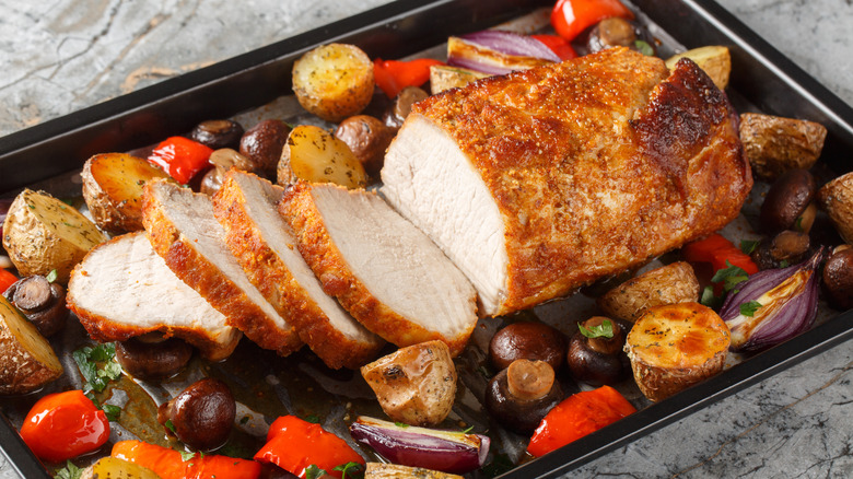a pork roast with a browned crust sliced on a tray with roasted vegetables