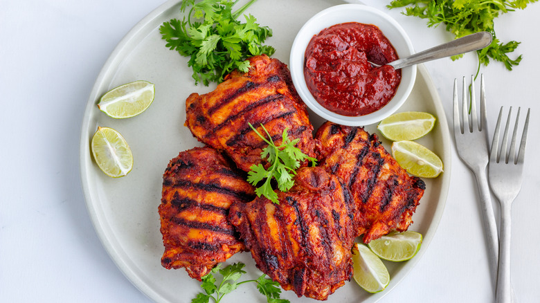 grilled marinated chicken thighs on a plate with sauce and limes