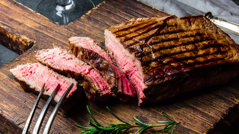 grilled top sirloin sliced on a wooden platter with a sprig of rosemary