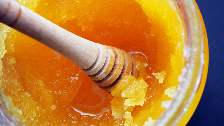 Wooden honey dipper in jar of crystallized honey