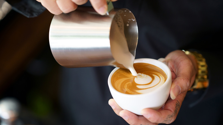 Pouring frothy milk into cup of coffee