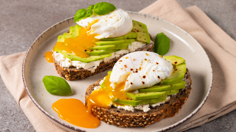 Two slices of toast topped with cream cheese, avocado slices, and poached eggs