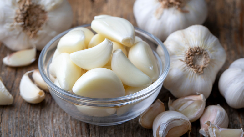 Peeled garlic cloves in small bowl next to whole bulbs of garlic
